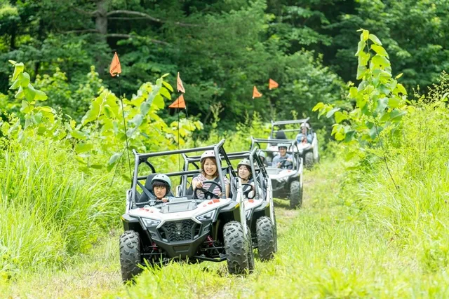 緑の草木が生い茂るゲレンデ跡のコースを一列に進む複数台のPolaris RZRバギー。先頭には母親と子どもが乗り、後続車両が続く。