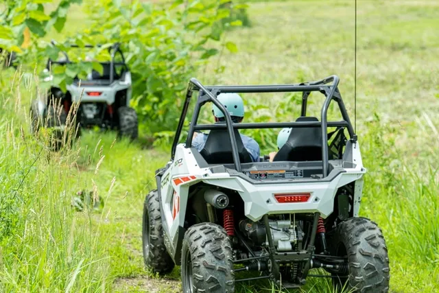 草が茂る夏のゲレンデ斜面を後方から捉えたPolaris RZRバギー2台。緑の草地と丘陵の地形がスキーコースの面影を残している。