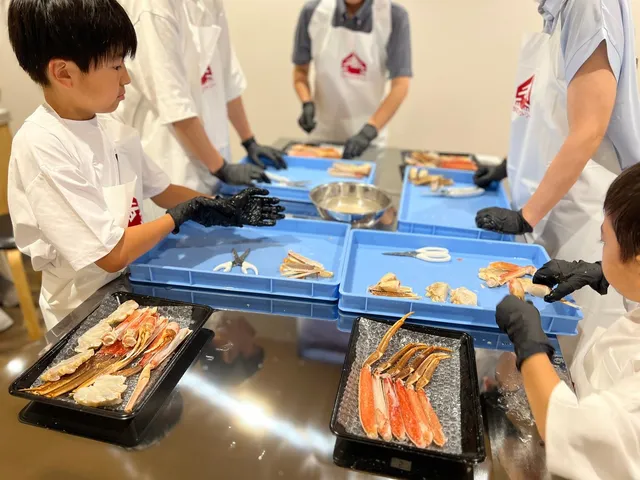 かにファクトリーの体験プログラムでカニの殻むきに取り組む子どもたちと、手元のトレーに並ぶカニの脚と身
