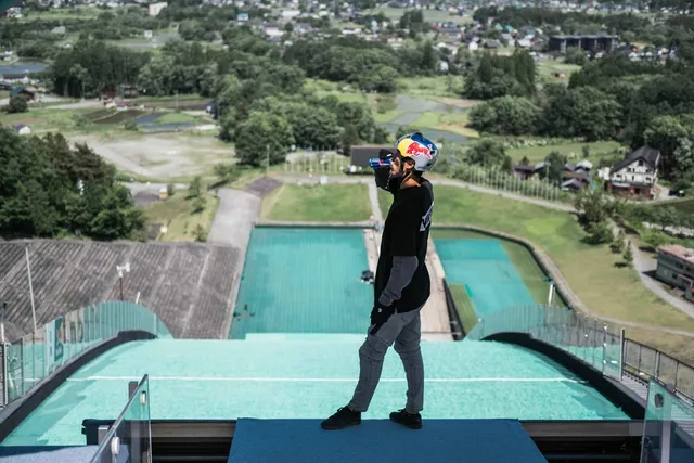 白馬ジャンプ競技場の頂上に立ち、眼下に広がるランディングバーンと白馬の街並みを見下ろしながら飲み物を飲む西窪友海さん
