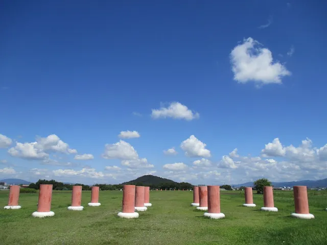 藤原宮跡に復元された朱色の列柱が緑の草原に並ぶ風景。背後に畝傍山と青空が広がり、建物は一切残っていない