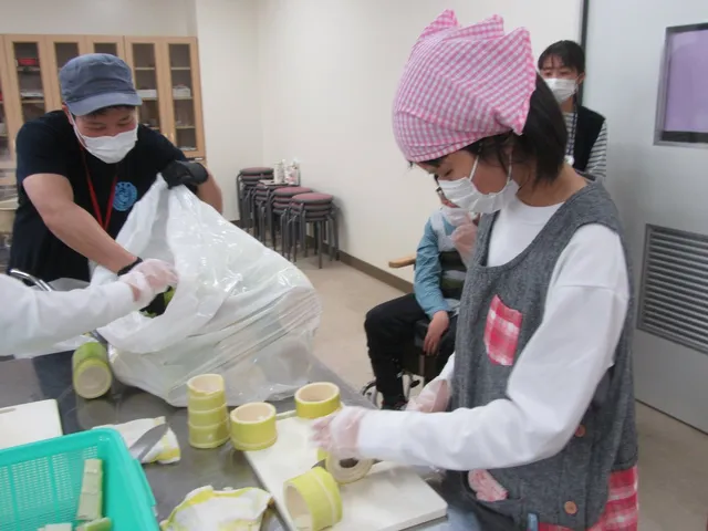 学校の調理室で幼竹を輪切りにする支援学校の生徒とスタッフ。まな板の上に切り分けられた幼竹の断面が並ぶ