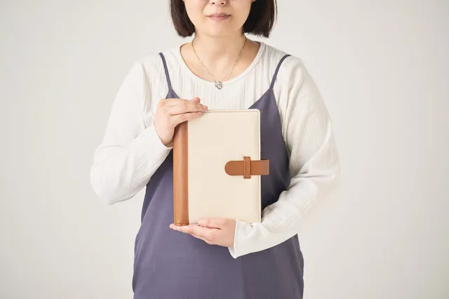 LIFERNY手帳のカバーを両手で胸の前に持つ女性。クリーム色の帆布とキャメルの革を組み合わせたシステム手帳カバー