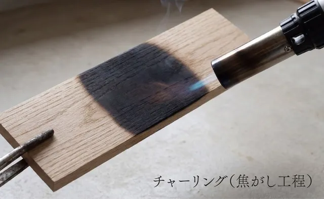 ミズナラ材の板をバーナーで焼き焦がすチャーリング（焦がし工程）の様子。木の表面が黒く炭化している