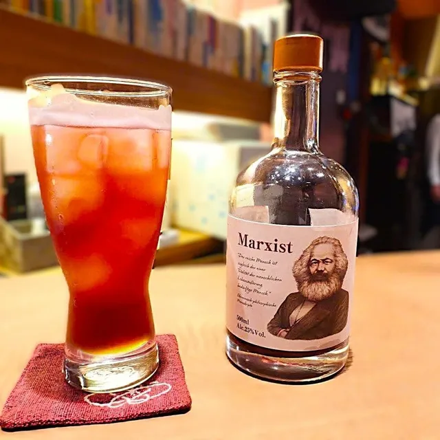 「Marxist」のボトルとグラスに注がれた深紅のリキュール。バーカウンターの上で氷入りのグラスが赤く輝いている