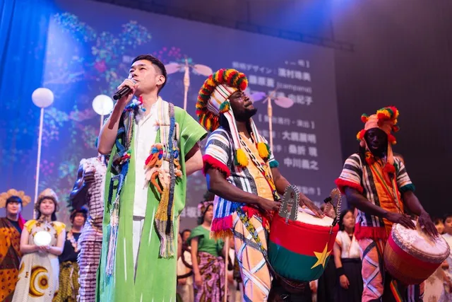 カラフルな民族衣装を着たブルキナファソの演者と太鼓を演奏する出演者、観客と共演するステージの様子
