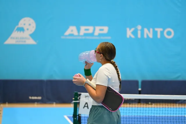 パデルまたはピックルボールの選手がピンクの断熱ボトルで水分補給する様子