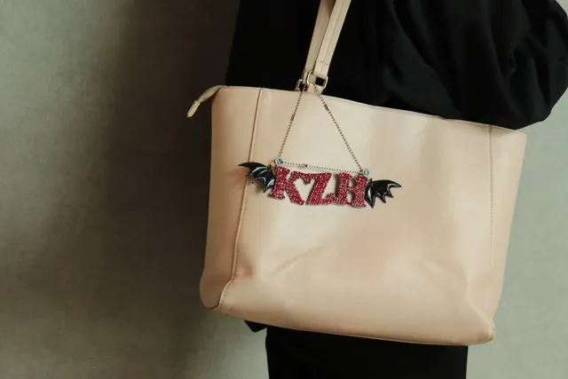 ラインストーンで飾られた『KZH』のイニシャルと蝙蝠の羽モチーフのストラップが、実際にトートバッグに取り付けられている様子