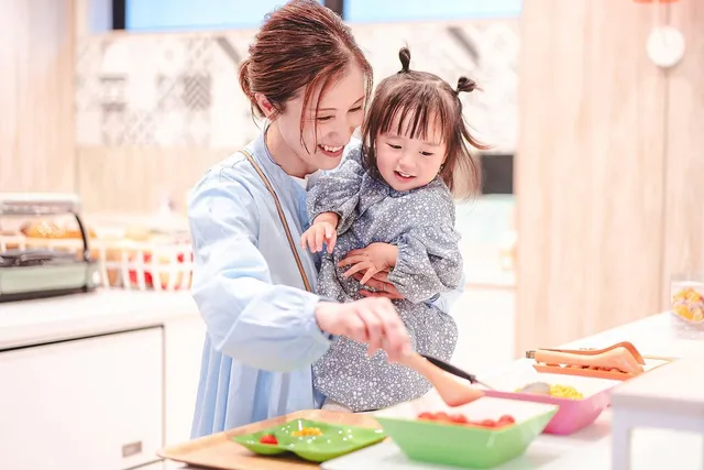 母親が幼い子どもを抱っこしながらホテルのキッチンスペースで料理を楽しむ様子