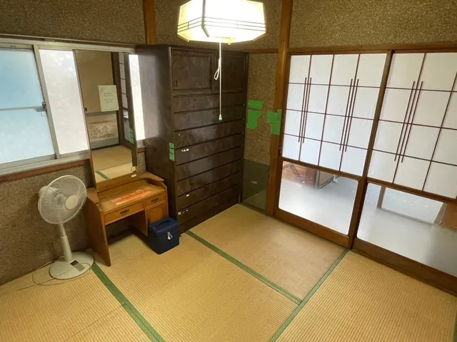 和室に置かれた古い鏡台とタンス、扇風機など、当時の生活用品がそのまま残された空き家の一室
