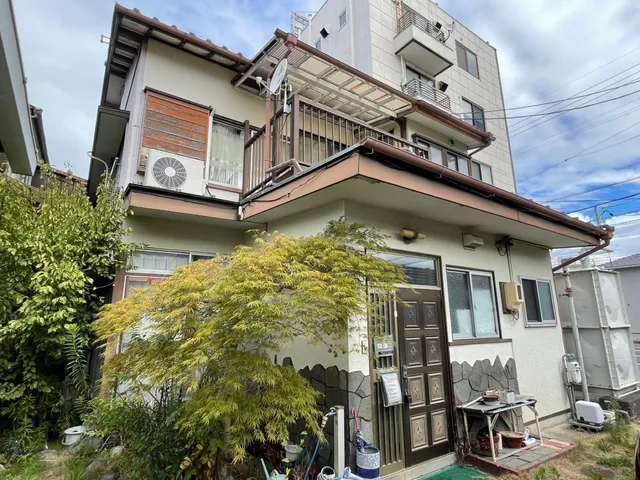会場となる静岡市の空き家の外観。3階建ての隣家に接する二階建て住宅で、バルコニーや植栽が見える