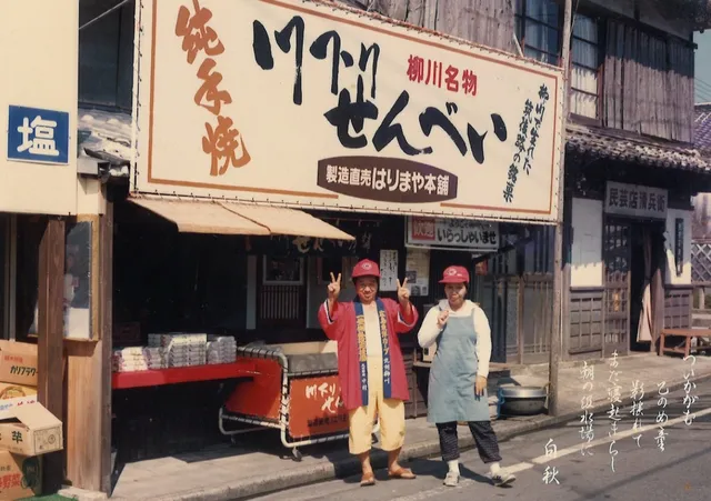 柳川名物「川下りせんべい」の看板を掲げたはりまや本舗の元店舗前で記念撮影する店主とスタッフ