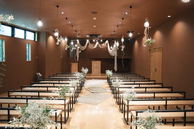 FOLK FOLKの挙式会場。木製ベンチが並ぶ温かみのある空間に白いドレープと照明が吊るされている