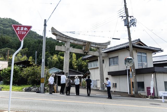 鳥居の前に集まり案内を聞く見学者たちと石工の里の街並み